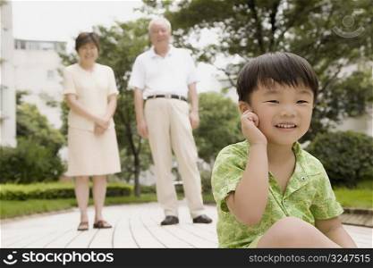 Portrait of a boy touching his ear with his grandparents standing behind him
