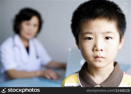 Portrait of a boy with a female doctor working on a laptop in the background