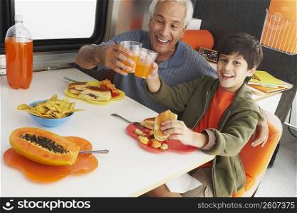 Portrait of a boy with his grandfather toasting glasses of juice
