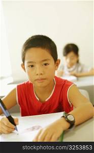 Portrait of a boy writing on a spiral notebook in the classroom