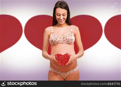 Portrait of a brunette, pregnant woman holding a flower heart