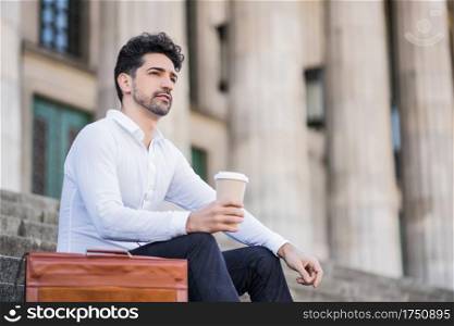 Portrait of a business man drinking a cup of coffee on a break from work while sitting on stairs outdoors. Business concept.