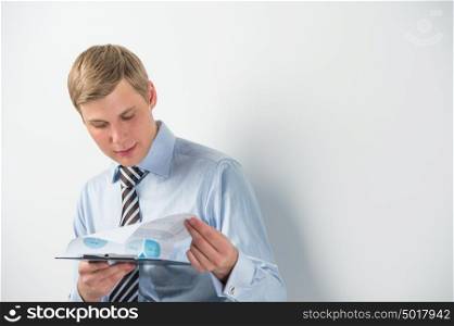 Portrait of a business man reading documents while leaning on the wall at his office