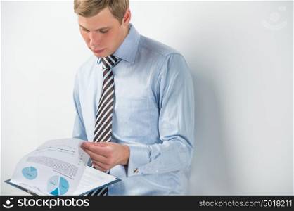 Portrait of a business man reading documents while leaning on the wall at his office