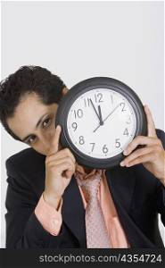 Portrait of a businessman hiding his face with a clock