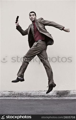 Portrait of a businessman holding a mobile phone and jumping