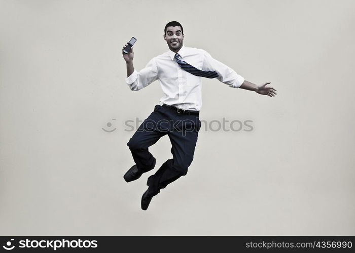 Portrait of a businessman holding a mobile phone and jumping