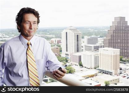 Portrait of a businessman holding a mobile phone with a city in the background