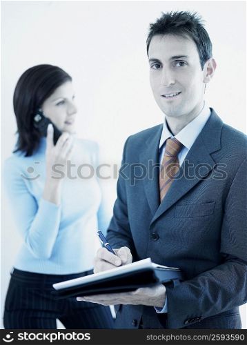 Portrait of a businessman holding a personal organizer with a businesswoman talking on a mobile phone in the background