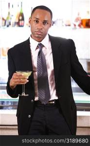 Portrait of a businessman leaning against a bar counter holding a martini glass