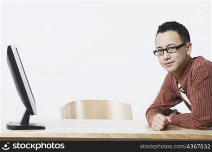 Portrait of a businessman leaning against a table in front of a flat screen monitor