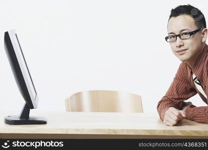 Portrait of a businessman leaning against a table in front of a flat screen monitor