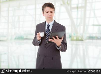 Portrait of a businessman looking at tablet pc and holding cup of coffee, at the office