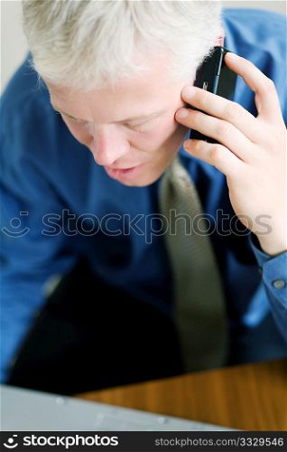 Portrait of a businessman on the phone, looking at the viewer over his laptop computer