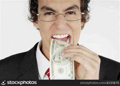 Portrait of a businessman putting a dollar bill into his mouth