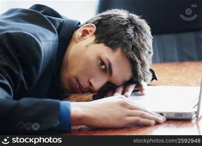 Portrait of a businessman resting his head on a desk in front of a laptop