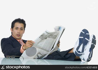 Portrait of a businessman resting his legs on the table and reading a newspaper