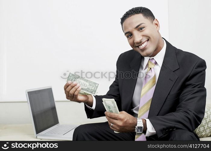 Portrait of a businessman sitting beside a laptop and counting paper currency