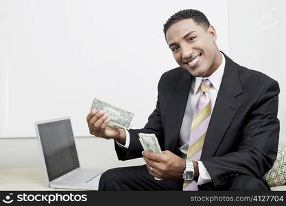 Portrait of a businessman sitting beside a laptop and counting paper currency