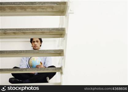 Portrait of a businessman sitting cross-legged on a step and holding a globe
