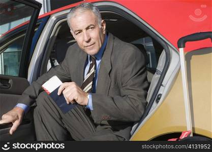 Portrait of a businessman sitting in a taxi with holding a passport and an airplane ticket