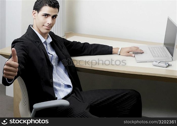 Portrait of a businessman sitting in front of a laptop and showing a thumbs up sign