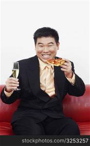 Portrait of a businessman sitting on a couch and holding a slice of pizza with a champagne flute
