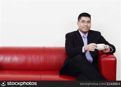 Portrait of a businessman sitting on a couch with a cup of tea and smiling