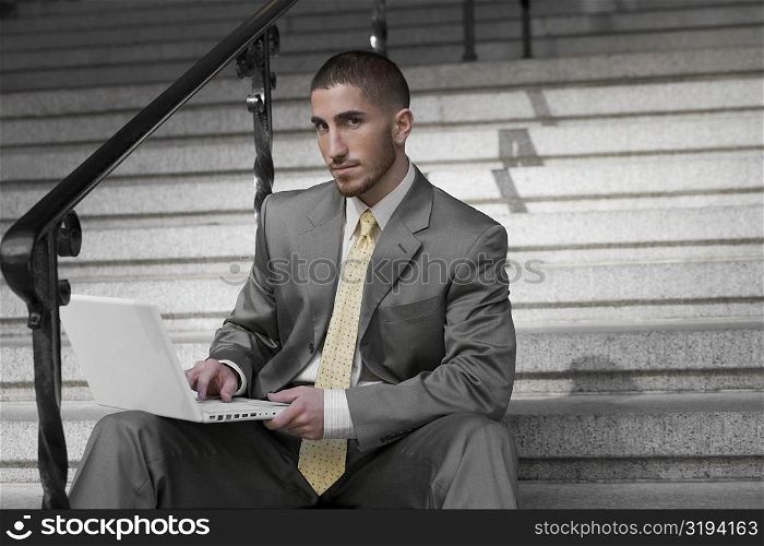 Portrait of a businessman sitting on a staircase and using a laptop
