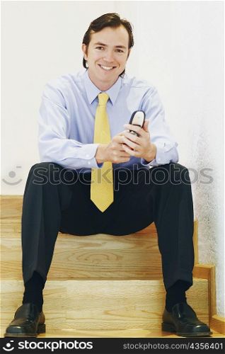 Portrait of a businessman sitting on a staircase and using a mobile phone