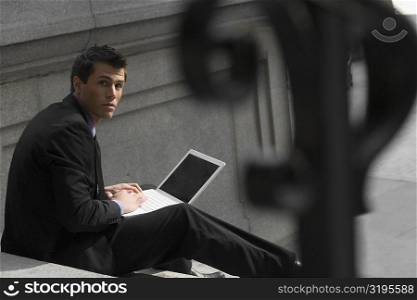 Portrait of a businessman sitting on steps and using a laptop