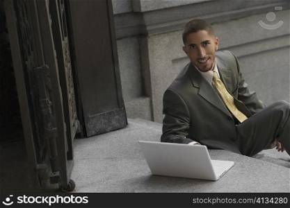 Portrait of a businessman sitting on steps and using a laptop