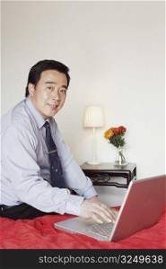 Portrait of a businessman sitting on the bed using a laptop