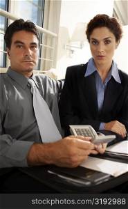 Portrait of a businessman sitting with a businesswoman holding a calculator