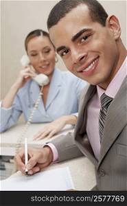 Portrait of a businessman smiling with a female receptionist talking on the telephone behind him