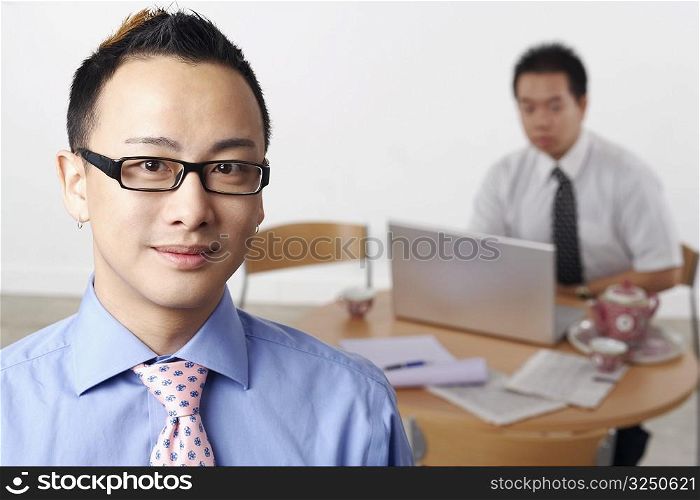 Portrait of a businessman smiling with another businessman using a laptop behind him