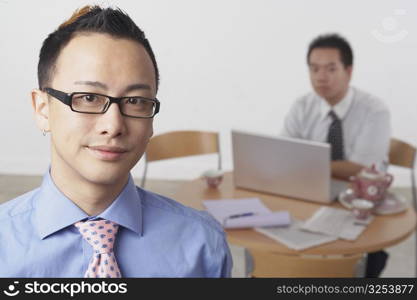 Portrait of a businessman smiling with another businessman using a laptop behind him