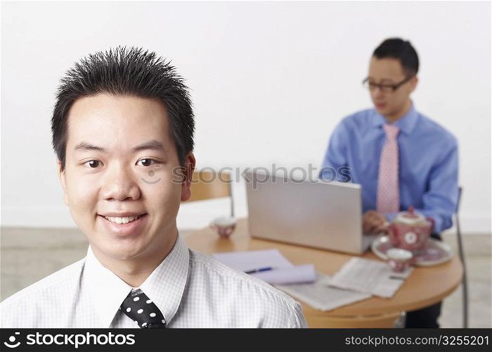 Portrait of a businessman smiling with another businessman using a laptop behind him