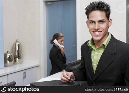 Portrait of a businessman standing at a hotel reception with a receptionist talking on the telephone behind him