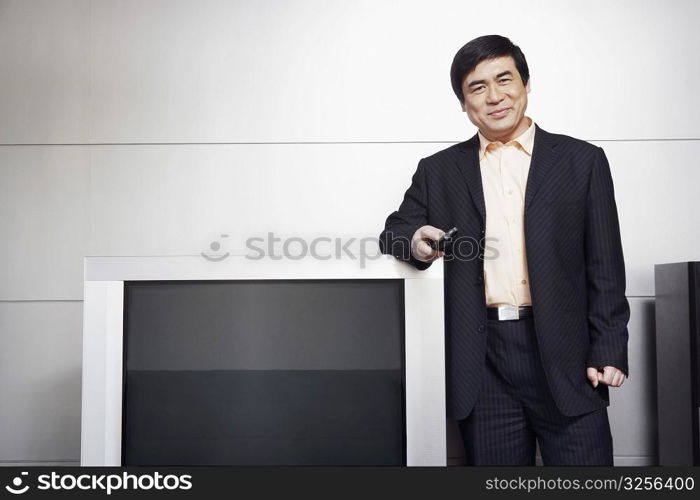 Portrait of a businessman standing by the side of a television smiling