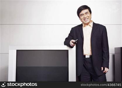 Portrait of a businessman standing by the side of a television smiling