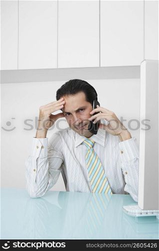 Portrait of a businessman talking on a mobile phone and thinking in an office