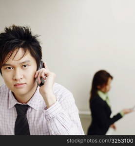 Portrait of a businessman talking on a mobile phone with a businesswoman in the background