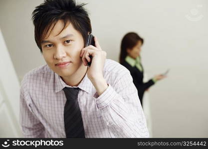 Portrait of a businessman talking on a mobile phone with a businesswoman in the background