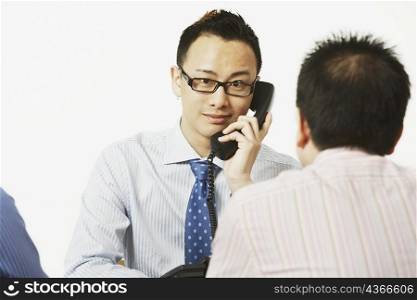 Portrait of a businessman talking on the telephone with two businessmen sitting in front of him