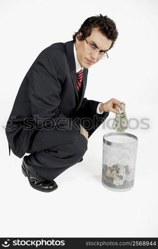 Portrait of a businessman throwing paper currency into a wastepaper basket