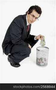 Portrait of a businessman throwing paper currency into a wastepaper basket