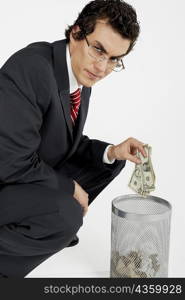 Portrait of a businessman throwing paper currency into a wastepaper basket