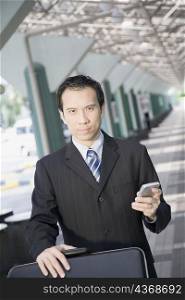 Portrait of a businessman using a palmtop and pushing a luggage cart