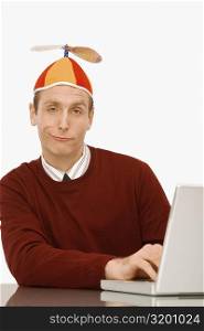 Portrait of a businessman wearing a propeller beanie and working on a laptop